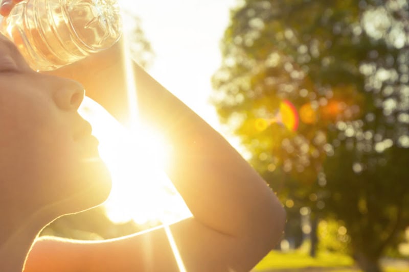 3 Tips to Prevent AC Breakdown During a Heat Wave Photo of a woman using a water bottle to cool off in the hot sun.